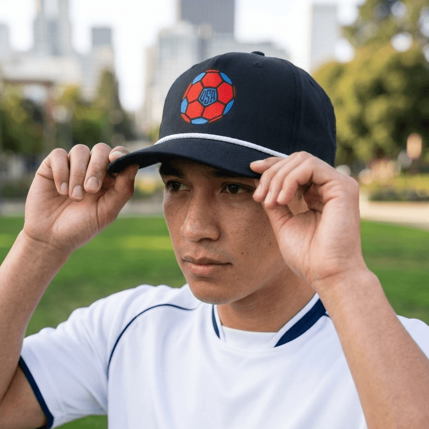 Person wearing a black cap with a colorful soccer ball logo in an outdoor setting