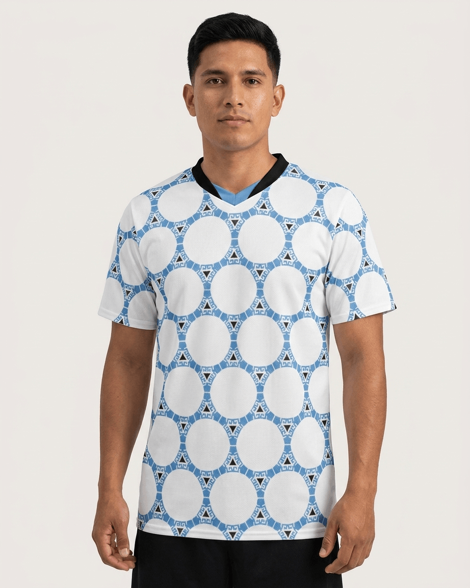 A man wearing a white short-sleeve V-neck soccer jersey with a blue geometric pattern, set against a plain light beige background.