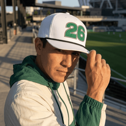 Person wearing a white cap with green number 26, standing on a stadium platform.
