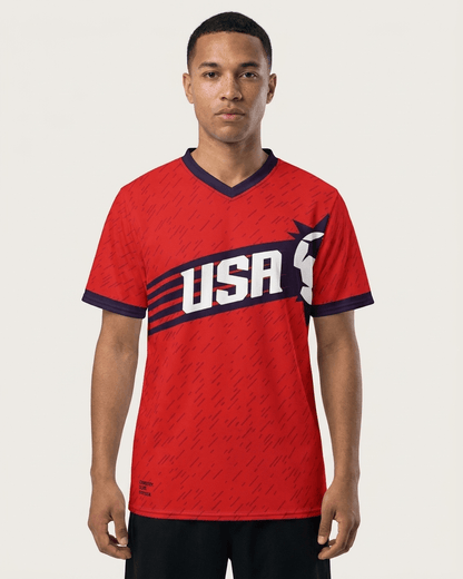 A man wearing a red short-sleeve V-neck jersey with navy blue trim and a large white USA graphic across the chest, photographed against a light gray studio background.