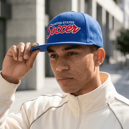 Man wearing a blue cap with 'United States Soccer' text in an urban setting