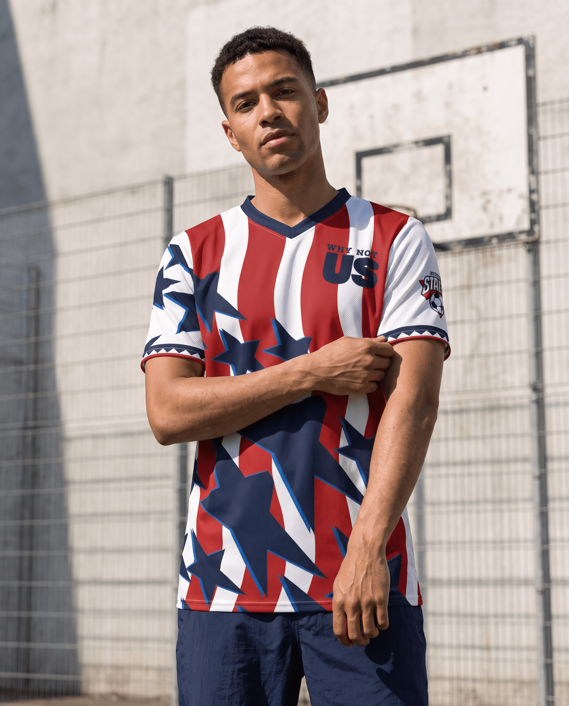 A man wearing a red, white, and blue soccer jersey with a geometric American flag pattern, standing in front of a concrete wall and basketball hoop.